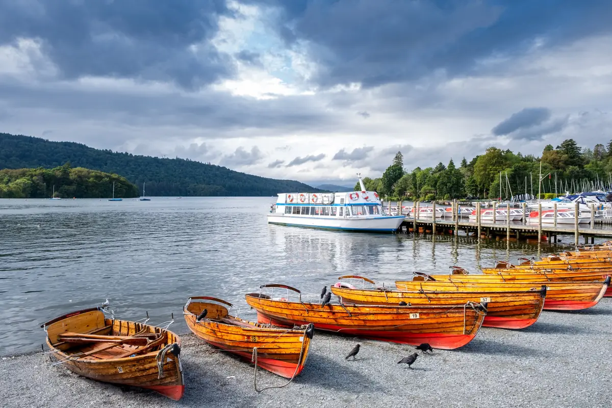 Wooden rowing boats on the shore at Bowness Bay, with a Windermere cruise boat at the pier