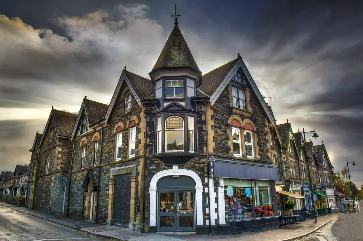 Victorian Lakeland stone shops with a pointed corner turret in Windermere village under a stormy sky